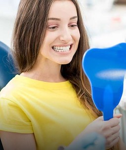woman looking at her teeth in a mirror sitting in a dental office